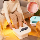 Bassine Bain de Pied blanche en bois, pieds immergés, femme assise sur canapé immerge les pieds; tablette téléphone posé, coussins pastel, image marketing du produit.

Note: ensure concise.