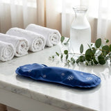 Poche gel bain dérivatif bleu avec motifs flocons, posée sur table en marbre, entourée de serviettes blanches et d’un carafe d’eau.